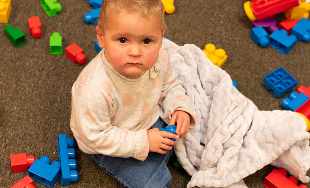 Toddler in blanket plays with blocks