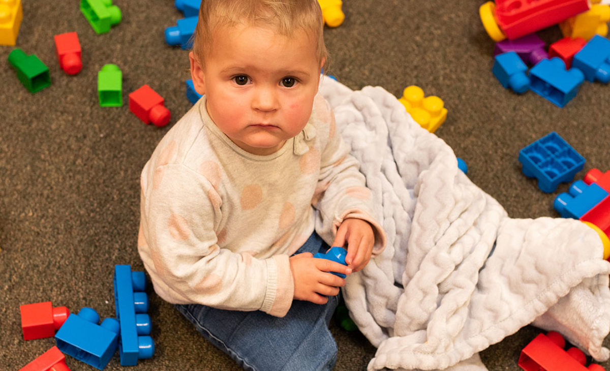 Toddler in blanket plays with blocks