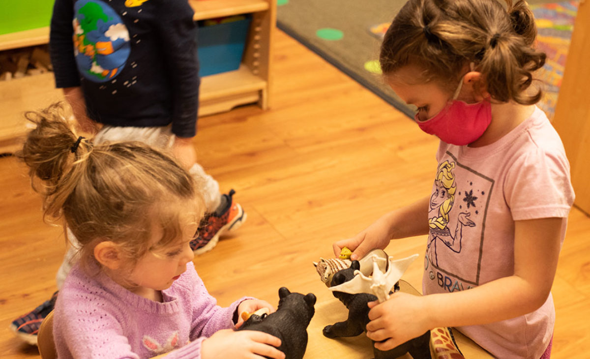 Two young girls play with animal toys