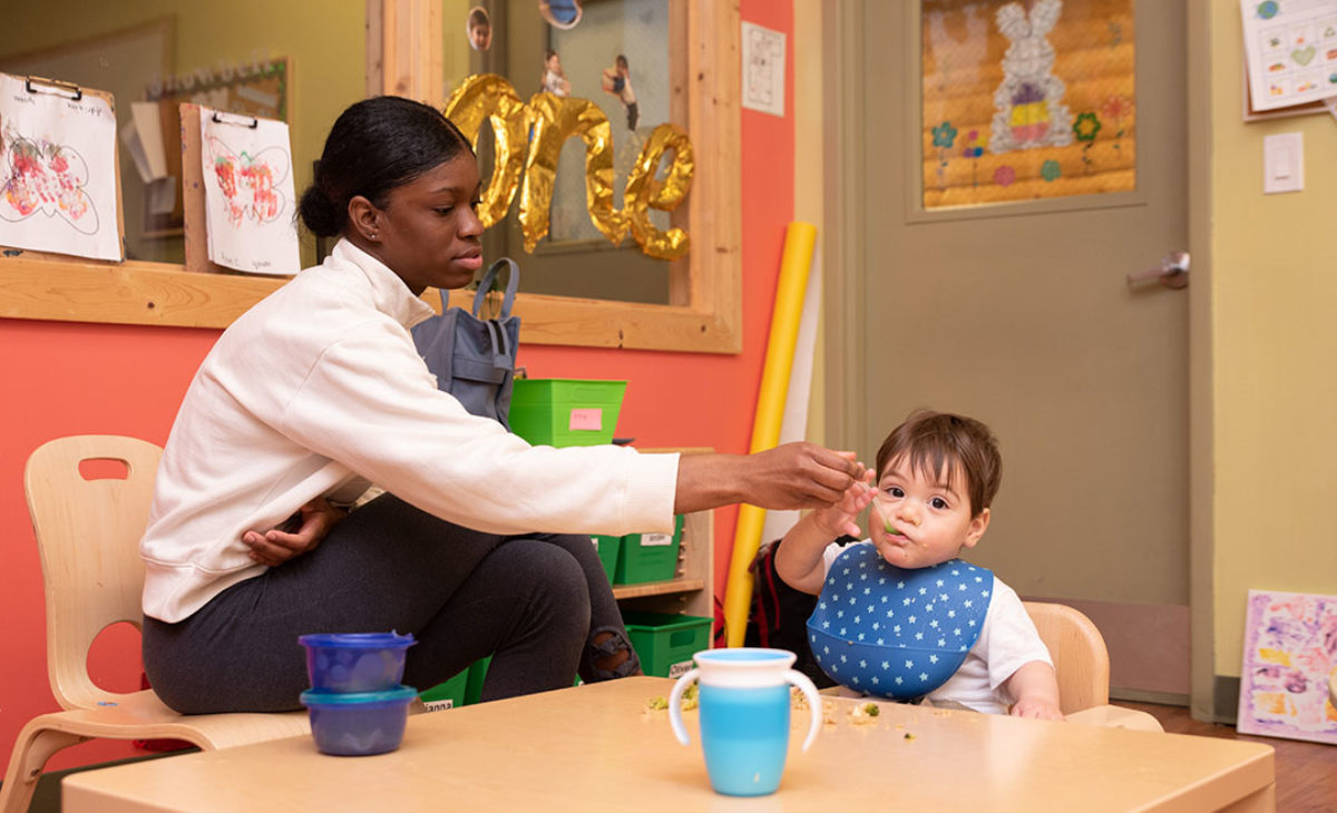 Toddler being fed by a young teacher at daycare