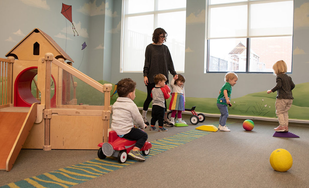 Teacher plays with young kids in daycare playroom
