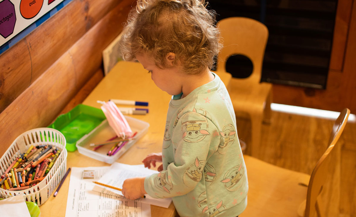 Toddler girl stands at drawing desk